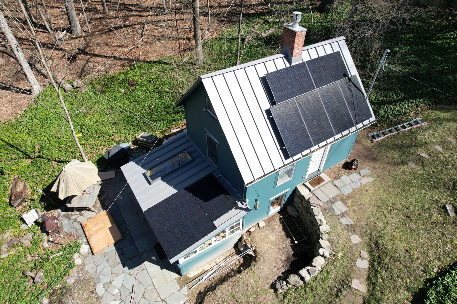 Solar panels on the metal roof of a blue cabin surrounded by woods