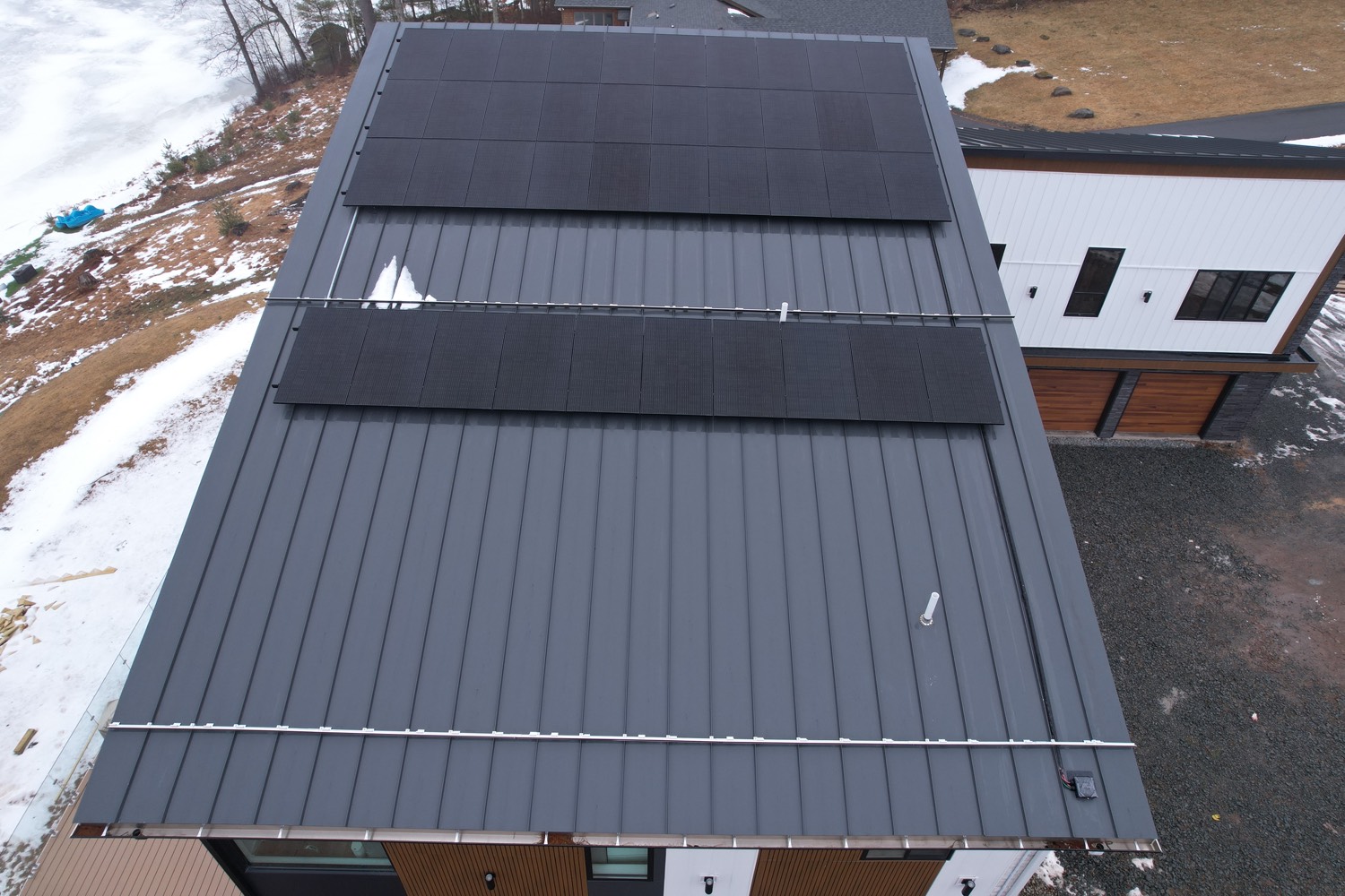 Sleek black solar panels on a dark standing-seam metal roof of a modern home
