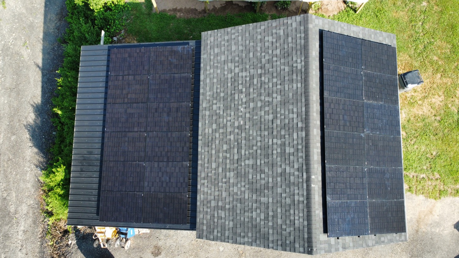 Aerial view of a black solar panel array on a gray shingle roof, green lawn in summer